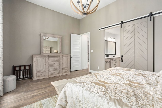 bedroom featuring a barn door, wood finished floors, a high ceiling, a chandelier, and ensuite bathroom
