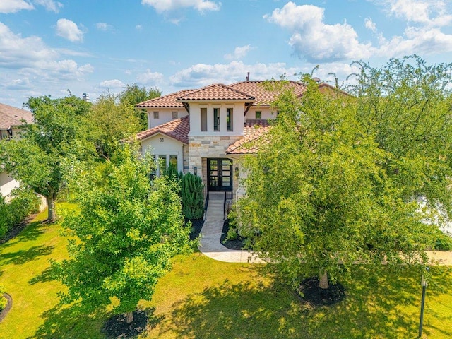 mediterranean / spanish house with stone siding, french doors, stucco siding, a tile roof, and a front yard