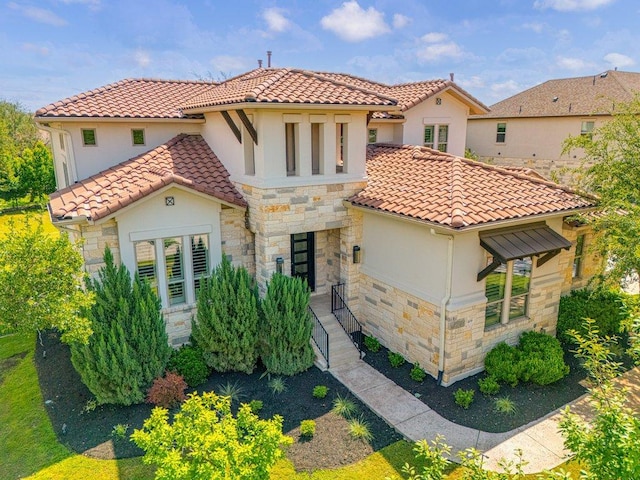 mediterranean / spanish-style home featuring stone siding, stucco siding, and a tiled roof