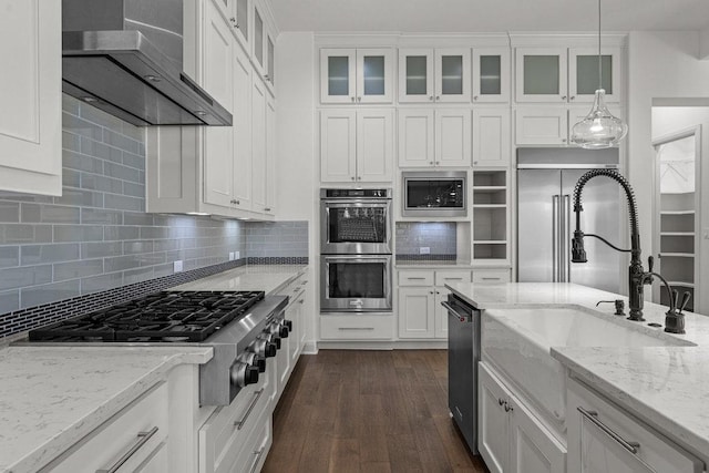 kitchen with appliances with stainless steel finishes, wall chimney range hood, a sink, white cabinetry, and decorative backsplash