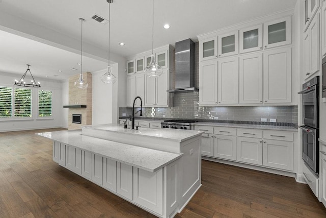 kitchen featuring wall chimney range hood, stainless steel appliances, white cabinetry, tasteful backsplash, and dark wood-type flooring