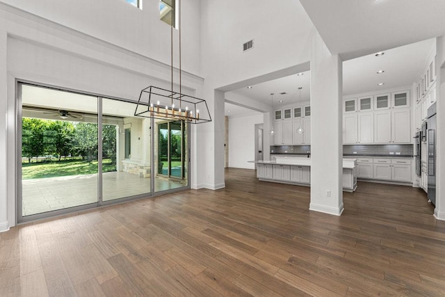 unfurnished living room with dark wood finished floors, a high ceiling, a chandelier, and baseboards