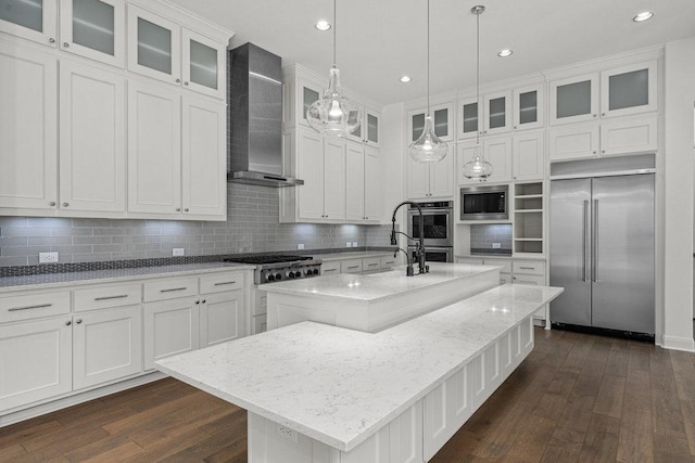 406 Woodside Ter, Austin, TX 78738 - kitchen featuring built in appliances, wall chimney exhaust hood, dark wood-style flooring, a center island with sink, and decorative backsplash