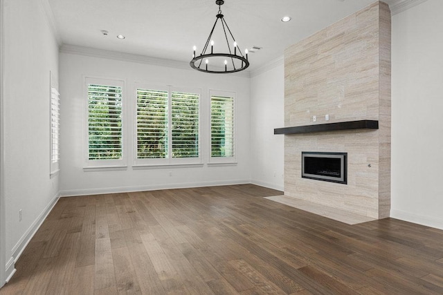 unfurnished living room featuring a chandelier, wood finished floors, crown molding, baseboards, and a tiled fireplace