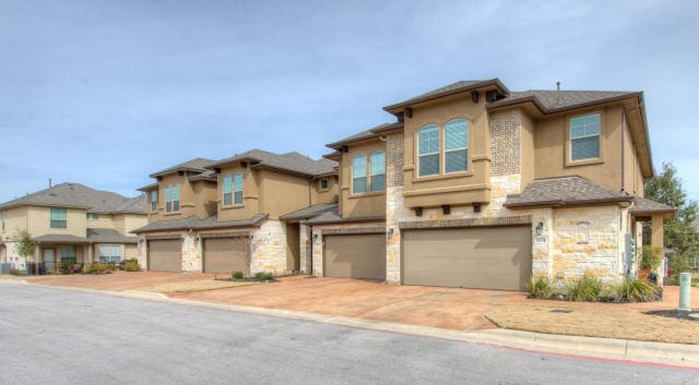 view of property featuring stone siding, an attached garage, stucco siding, and concrete driveway
