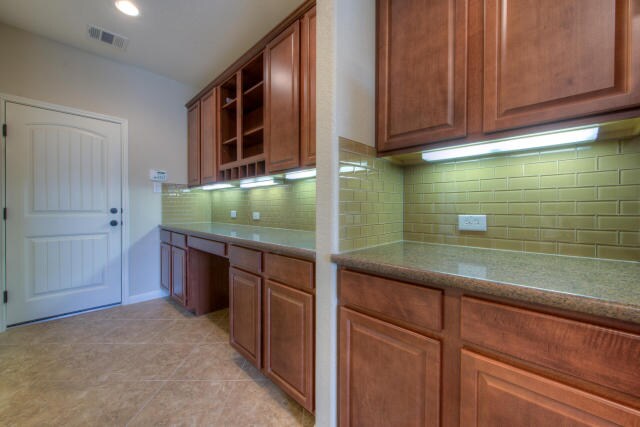 kitchen with open shelves, tasteful backsplash, brown cabinetry, and light tile patterned flooring