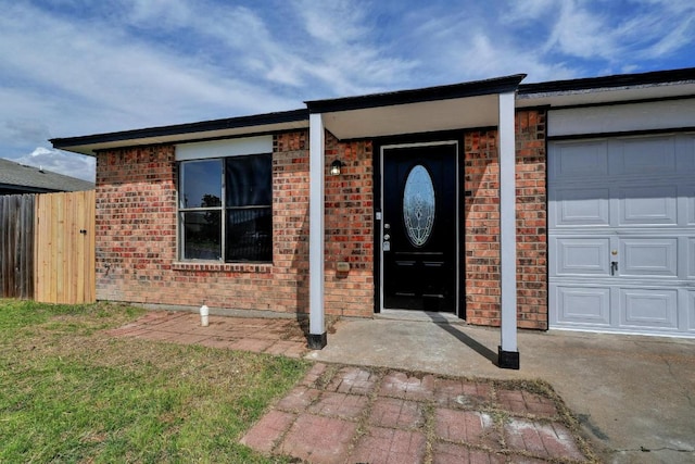entrance to property with fence, brick siding, and a garage