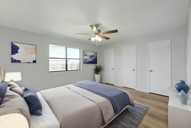 bedroom with light wood-type flooring, ceiling fan, and two closets