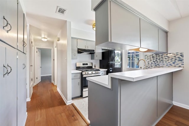 8500 Woodstone Dr, Austin, TX 78757 - kitchen with stainless steel range with gas stovetop, under cabinet range hood, freestanding refrigerator, gray cabinetry, and a peninsula