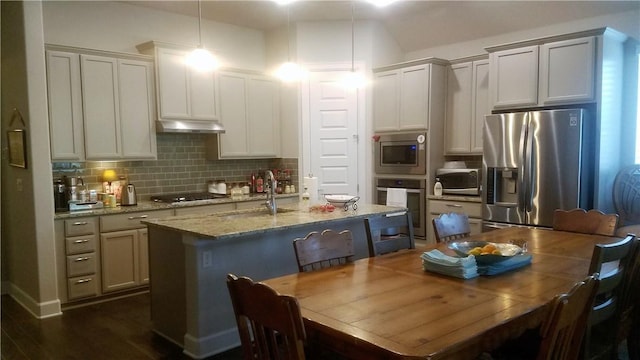 5301 Ponte Tresa Dr, Bee Cave, TX 78738 - kitchen with appliances with stainless steel finishes, under cabinet range hood, decorative backsplash, a kitchen island with sink, and light stone counters
