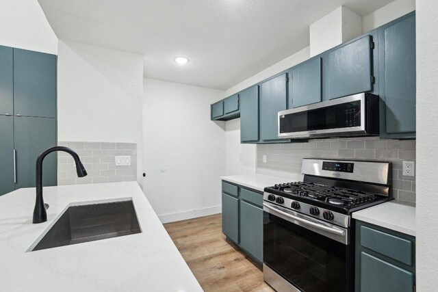 kitchen with appliances with stainless steel finishes, a sink, light countertops, backsplash, and light wood finished floors