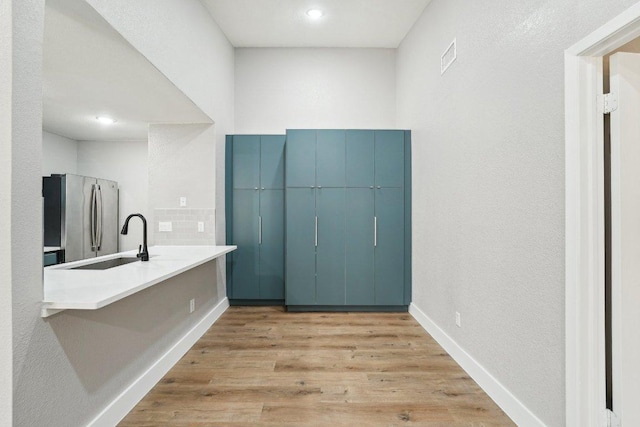 bar area with freestanding refrigerator, a sink, light wood finished floors, baseboards, and recessed lighting