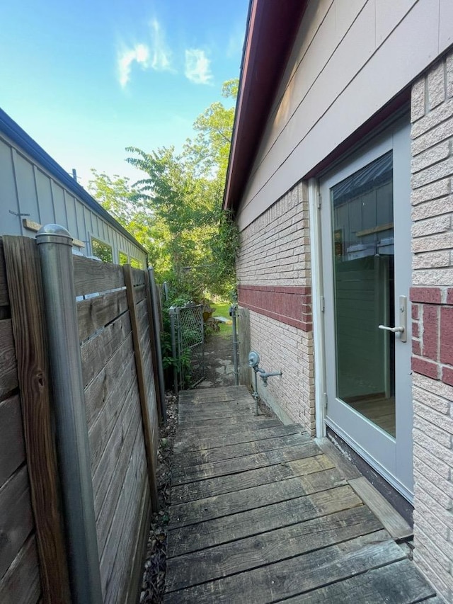 view of side of home with brick siding, a wooden deck, and fence
