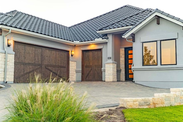 view of front of property featuring stone siding, an attached garage, stucco siding, and a tile roof