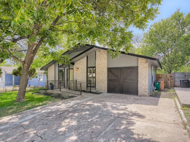 view of front of property with concrete driveway, central air condition unit, an attached garage, stone siding, and fence
