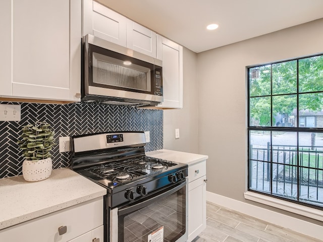 kitchen featuring stainless steel microwave, gas range oven, decorative backsplash, white cabinetry, and recessed lighting