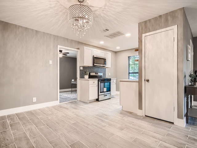kitchen featuring stainless steel appliances, white cabinetry, wood finish floors, baseboards, and a chandelier