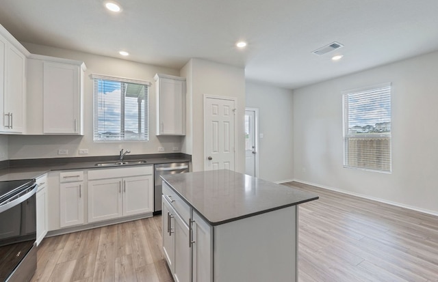 kitchen featuring appliances with stainless steel finishes, a sink, dark countertops, light wood-style flooring, and recessed lighting