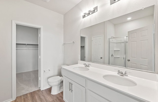 bathroom with wood finished floors, a shower stall, toilet, a walk in closet, and double vanity