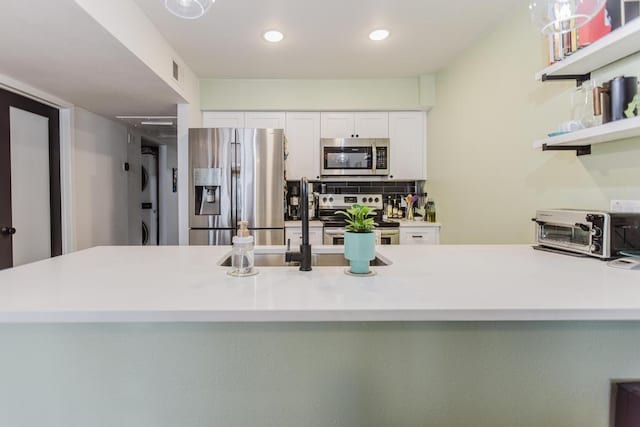 909 Reinli St Unit 102, Austin, TX 78751 - kitchen with appliances with stainless steel finishes, stacked washer and clothes dryer, white cabinetry, light countertops, and tasteful backsplash