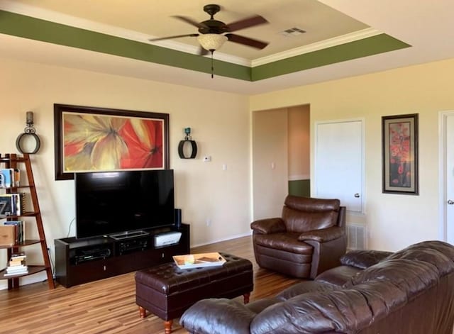 living room with a ceiling fan, wood finished floors, crown molding, and a raised ceiling