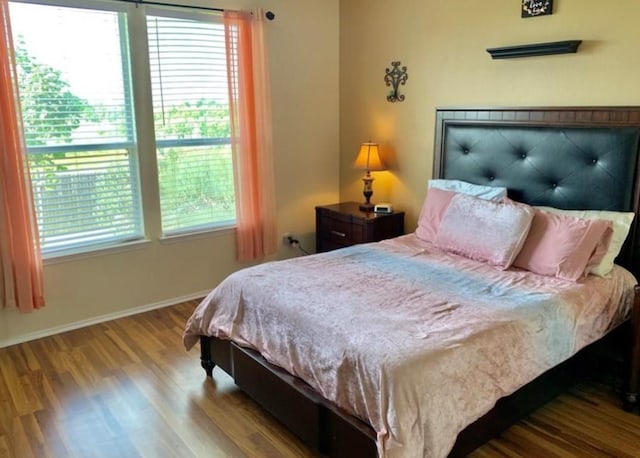 bedroom with multiple windows, wood finished floors, and baseboards