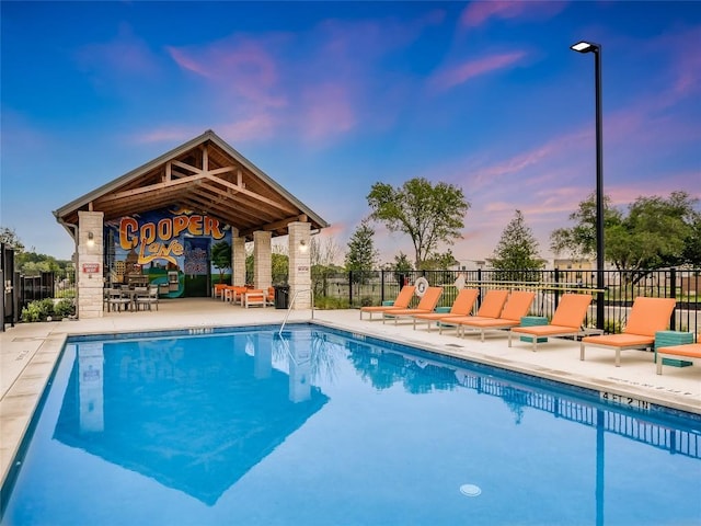 pool at dusk featuring fence, a community pool, a patio area, and a gazebo