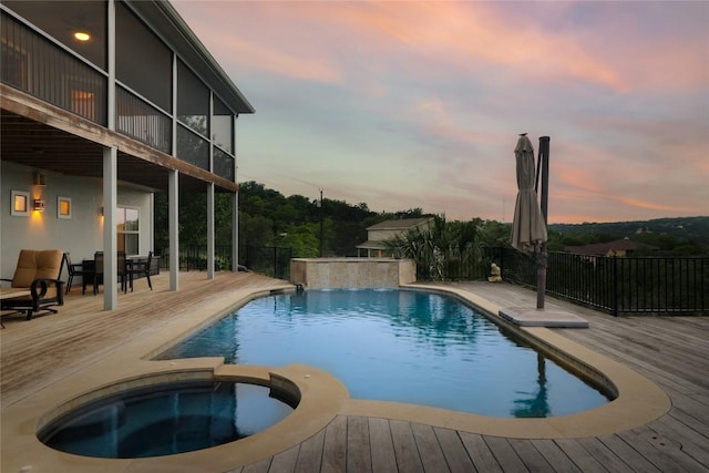 pool at dusk featuring a deck and a pool with connected hot tub