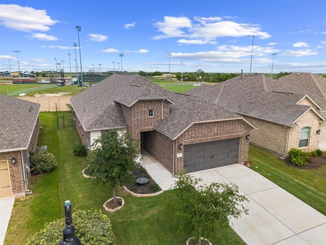 view of front facade featuring brick siding, an attached garage, a shingled roof, a front yard, and concrete driveway