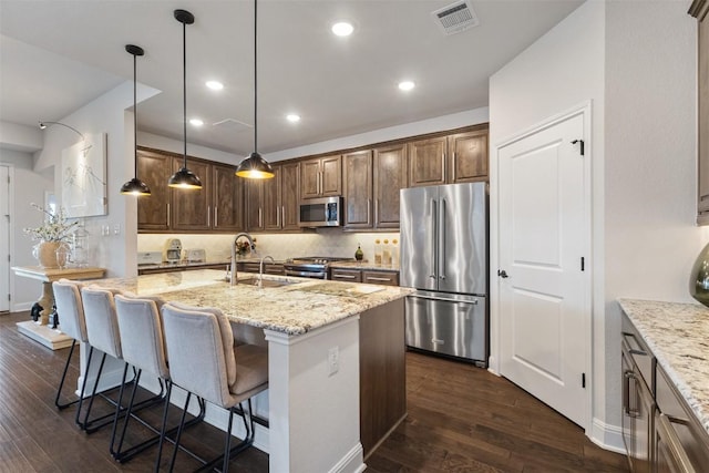 kitchen with stainless steel appliances, a sink, light stone counters, dark wood-type flooring, and recessed lighting