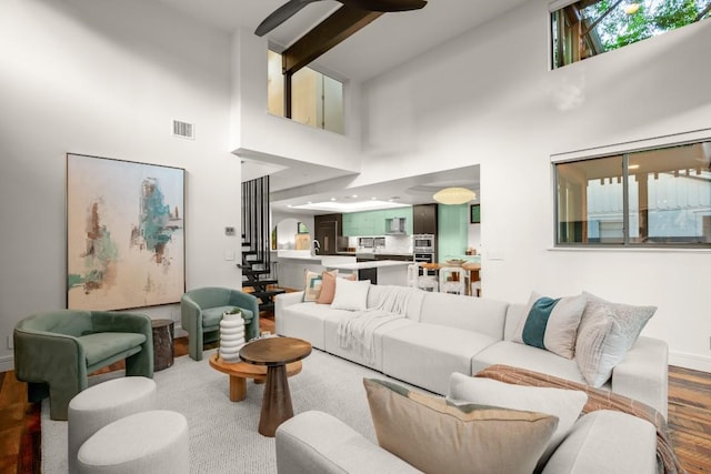 living room with a towering ceiling, stairway, wood finished floors, beamed ceiling, and baseboards