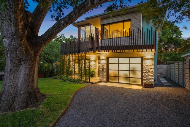 view of front of property with stone siding, a garage, driveway, and a balcony