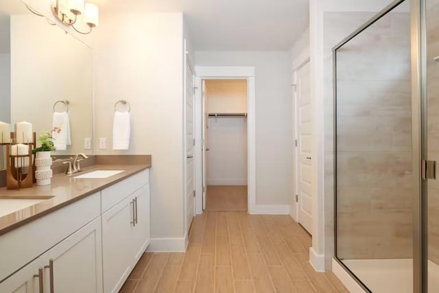 full bath featuring a shower stall, double vanity, a walk in closet, and baseboards