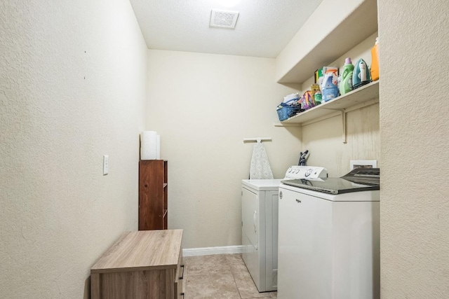 laundry area with washing machine and clothes dryer, baseboards, light tile patterned flooring, and a textured wall
