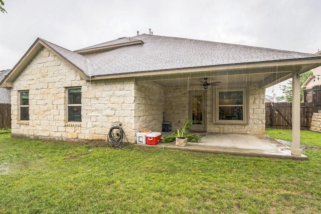 back of property with ceiling fan, a patio area, a shingled roof, and stone siding
