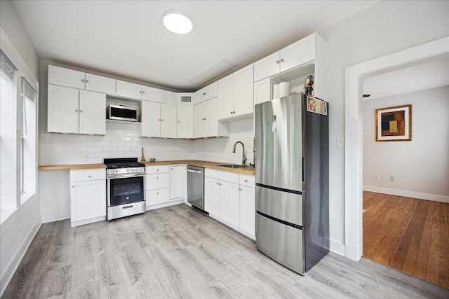 kitchen featuring stainless steel appliances, a sink, light wood-type flooring, wooden counters, and baseboards