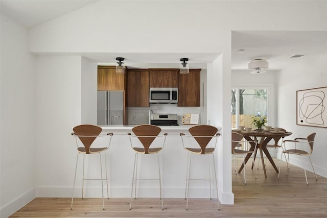 1800 Nicole Cir, Round Rock, TX 78664 - kitchen featuring stainless steel appliances, light countertops, a kitchen breakfast bar, brown cabinetry, and light wood-style floors