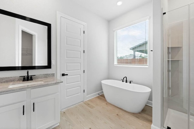 106 Nandina Path, Bastrop, TX 78602 - bathroom featuring wood finished floors, a stall shower, vanity, a freestanding bath, and baseboards