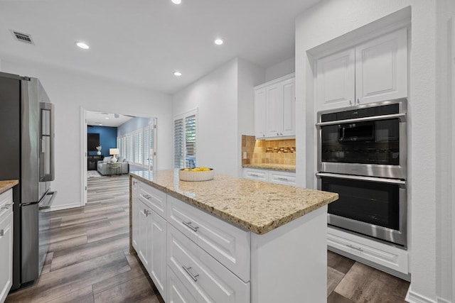 906 Texas Trl, Austin, TX 78737 - kitchen with appliances with stainless steel finishes, dark wood-style flooring, a center island, white cabinets, and light stone counters