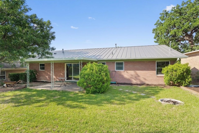 rear view of property featuring a patio area, brick siding, a yard, and metal roof