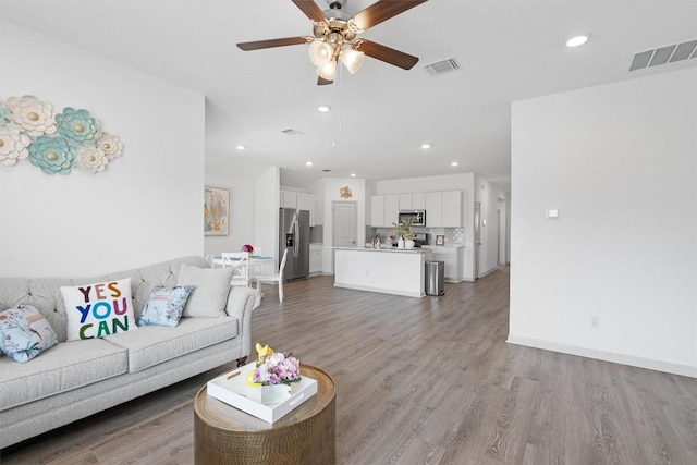 living area with ceiling fan, recessed lighting, light wood-type flooring, and baseboards
