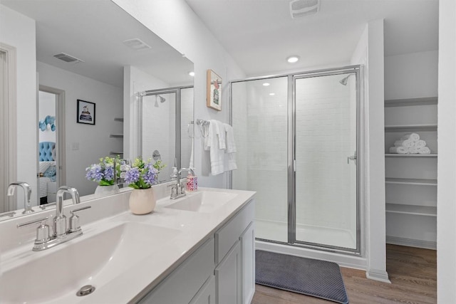 bathroom featuring wood finished floors, a stall shower, double vanity, and recessed lighting