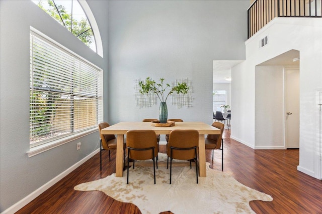 dining space with baseboards, a towering ceiling, plenty of natural light, and wood finished floors
