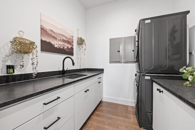 laundry area with estacked washer and dryer, cabinet space, wood finished floors, electric panel, and baseboards