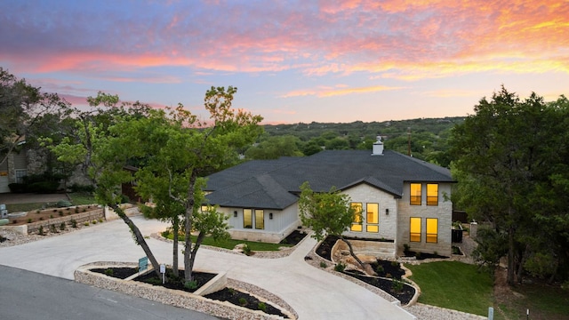 view of front of home featuring stone siding, curved driveway, a chimney, and a shingled roof