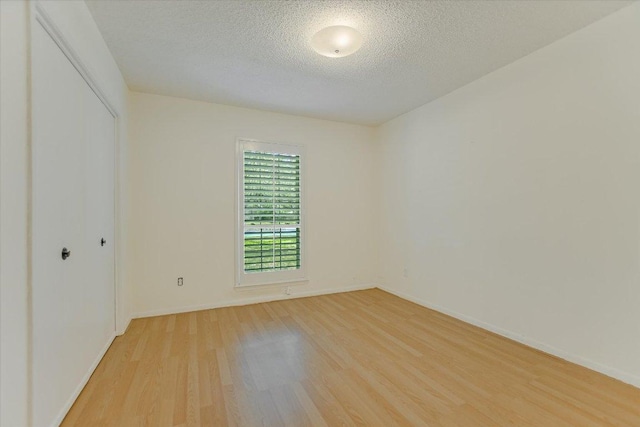 empty room with light wood finished floors, a textured ceiling, and baseboards