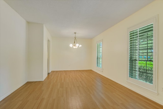 unfurnished room with light wood-style flooring, a chandelier, and baseboards