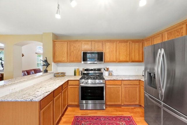 2111 Marcus Abrams Blvd, Austin, TX 78748 - kitchen featuring stainless steel appliances, light wood-style flooring, arched walkways, a peninsula, and light stone countertops