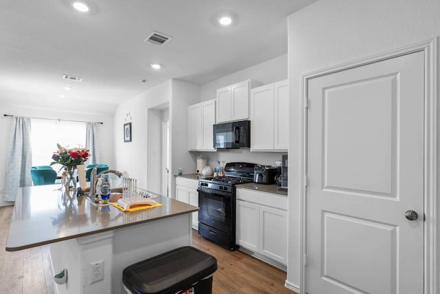 112 Montego St, Hutto, TX 78634 - kitchen with black appliances, wood finished floors, white cabinets, a kitchen island with sink, and recessed lighting