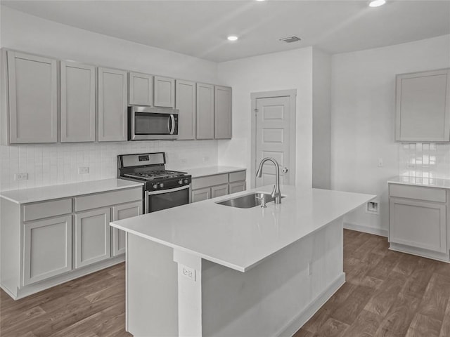 kitchen featuring stainless steel appliances, a sink, gray cabinets, dark wood-style floors, and recessed lighting